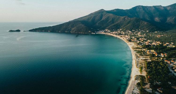 Panorama aérien d'une plage de sable fin majestueuse et d'une mer d'émeraude bordée par les montagnes couvertes de pins à Thassos.