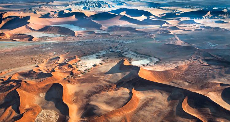 Stunning aerial view of sweeping orange sand dunes with intricate shadows across a vast desert basin.