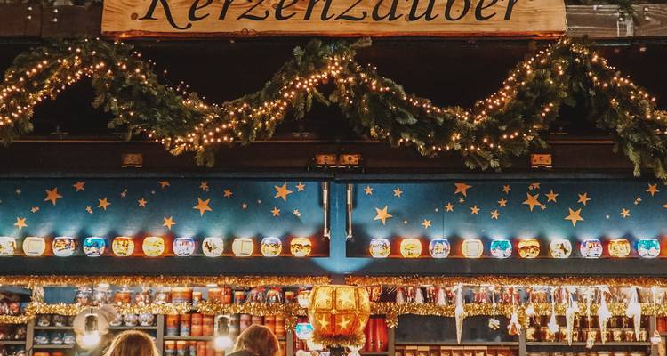 Étal du marché de Noël festif orné de guirlandes de conifères et de décorations illuminées par des bougies.