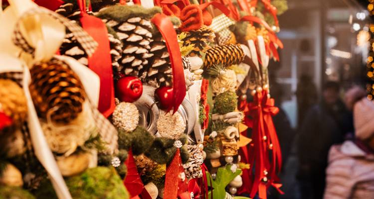 Gros plan d'objets artisanaux de Noël colorés avec des rubans, des pommes de pin et des ornements suspendus dans un étal de marché.