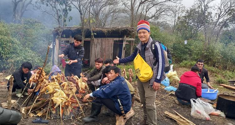 Des voyageurs rôtissant des poulets sur un feu de camp ouvert à côté d'une cabane en bois rustique en montagne