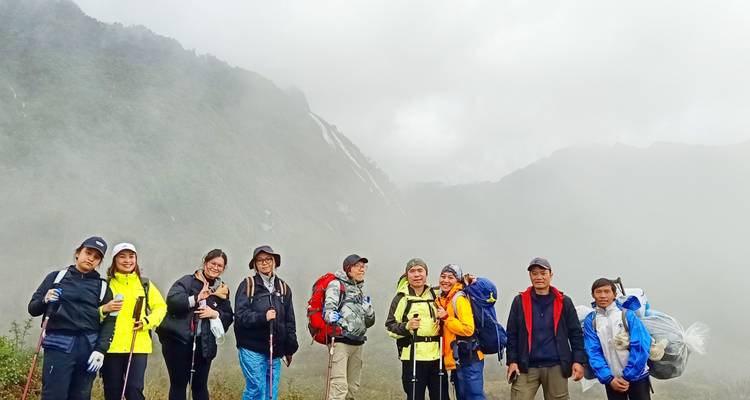 Grand groupe de randonneurs posant avec leurs sacs à dos à un col de montagne brumeux