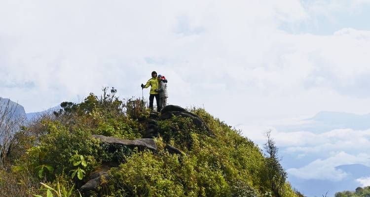 Deux trekkers se tiennent debout sur une crête étroite et verdoyante au-dessus d'une mer de nuages