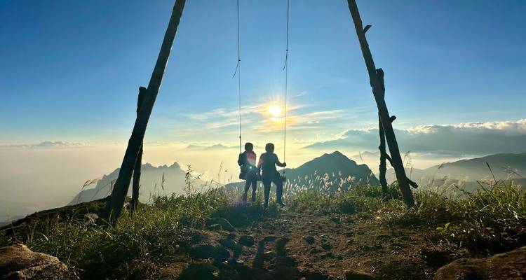 Deux enfants sur une structure de balançoire en bois se découpant en silhouette contre le soleil couchant haut dans les montagnes