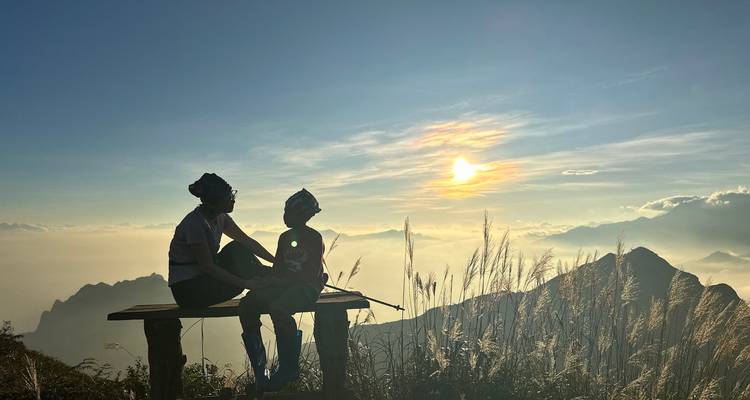 Un couple partage un banc donnant sur des pics brumeux et un soleil du soir étincelant
