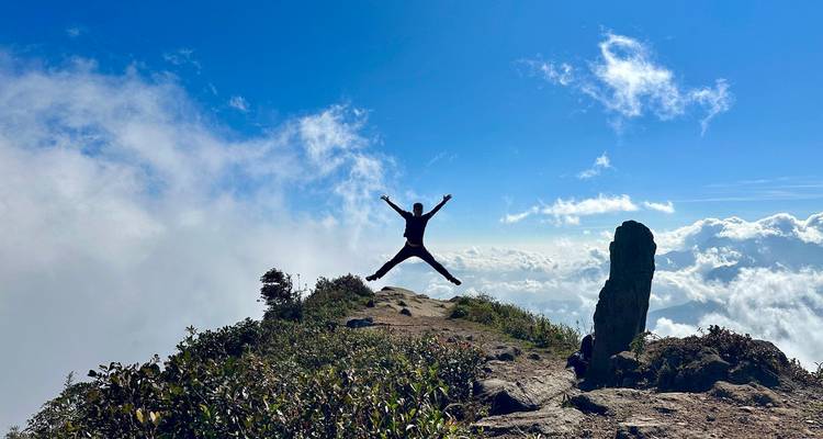 L'aventurier effectue un saut en étoile au bord de la falaise haut au-dessus des nuages roulants et du ciel bleu