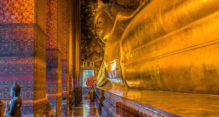 Bouddha doré couché du Wat Pho illuminé à l'intérieur d'une salle de temple richement décorée.