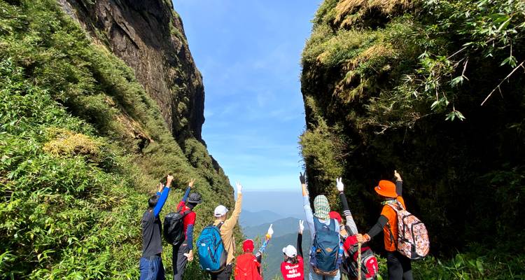 Groupe de randonneurs célébrant entre deux falaises imposantes, pointant du doigt vers la vue lointaine sous des ciels d'un bleu éclatant.