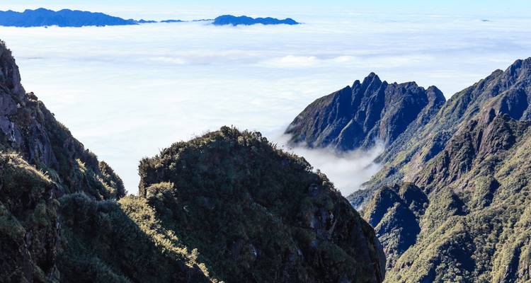 Des pics rocheux déchiquetés s'élèvent au-dessus d'une mer de nuages avec des crêtes lointaines s'estompant à l'horizon.