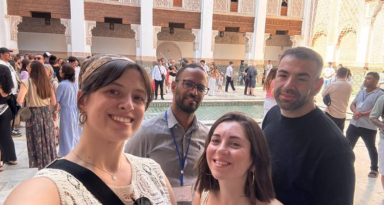 Selfie de groupe à l'intérieur d'une cour historique avec des arches ornées et un bassin réfléchissant entouré d'autres visiteurs.