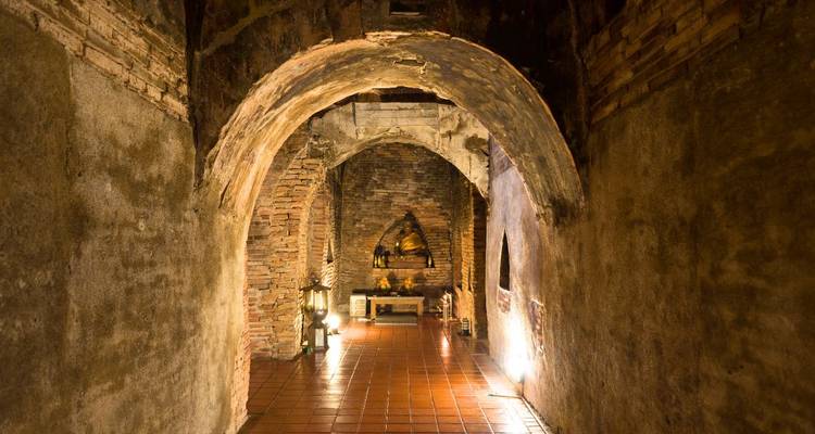 Corridor de tunnel en briques faiblement éclairé à l'intérieur d'un temple ancien avec une statue de Bouddha à l'extrémité.