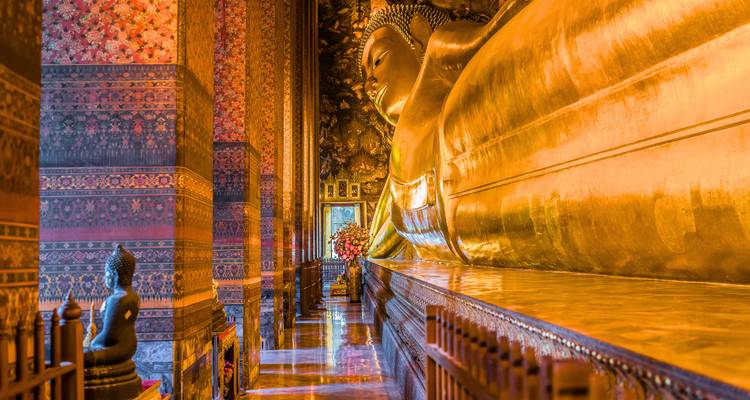 La statue dorée du Bouddha couché brille à l'intérieur d'une salle de temple ornementée avec des motifs élaborés.