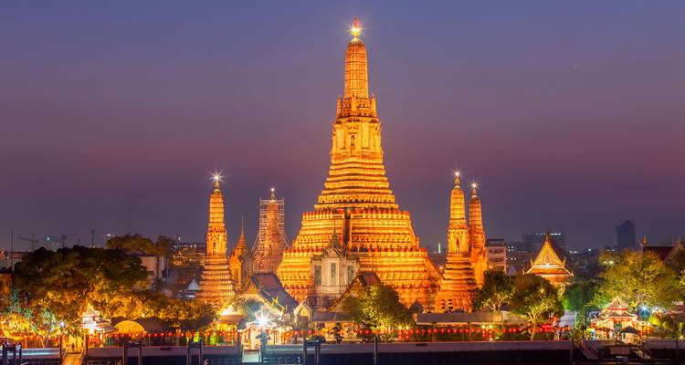 Le Wat Arun et ses flèches sont illuminés par des lumières orange sur un ciel crépusculaire violet.