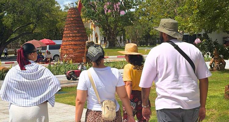 Quatre touristes se dirigent vers une petite stupa en briques dans un parc ensoleillé avec des arbres et du gazon.
