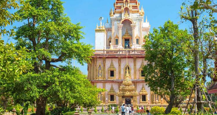 Une tour de temple thaï ornée s'élève au-dessus de jardins entretenus tandis que les visiteurs explorent les lieux.