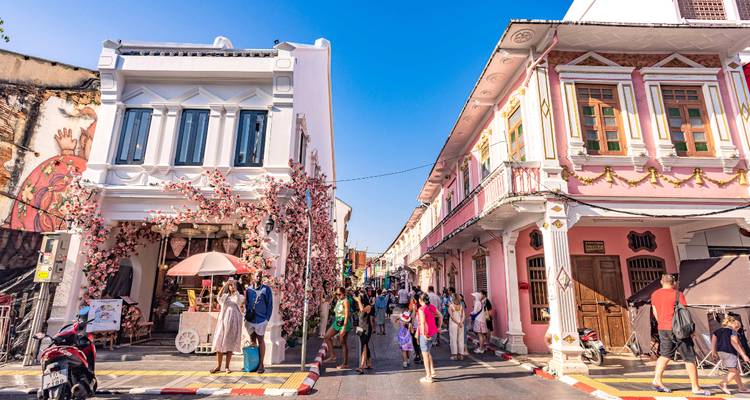 Des maisons de boutiques coloniales aux couleurs vives encadrent une rue piétonnière animée remplie de visiteurs sous un ciel bleu.