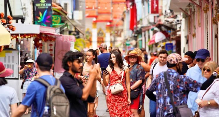 Des foules de visiteurs se déplacent dans une rue étroite et animée, bordée de façades de boutiques colorées et de décorations.
