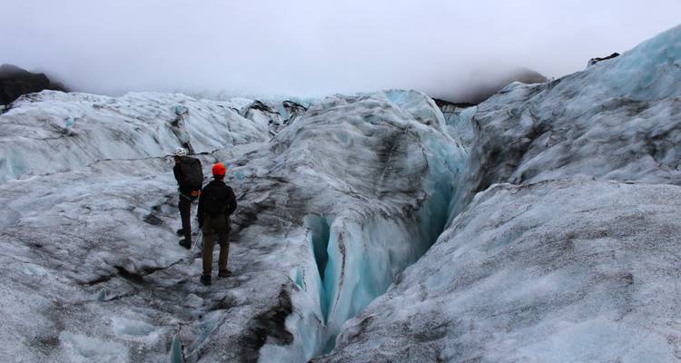 Les aventuriers portant des casques naviguent dans de profondes crevasses sur la glace aux stries bleues du glacier Solheimajokull.