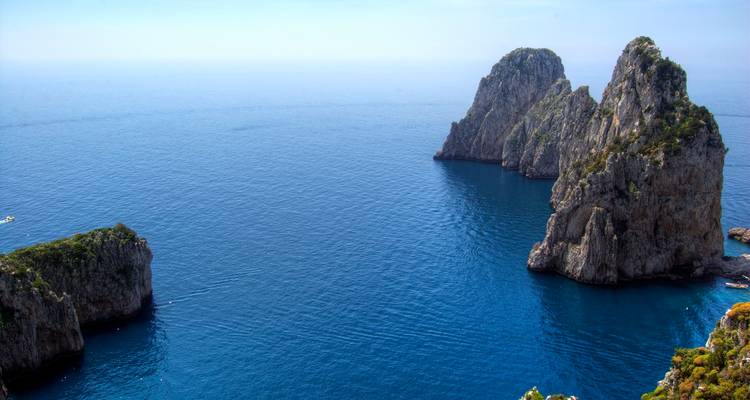 Les emblématiques formations rocheuses Faraglioni s'élevant des eaux d'un bleu profond au large de la côte de Capri par une journée dégagée.