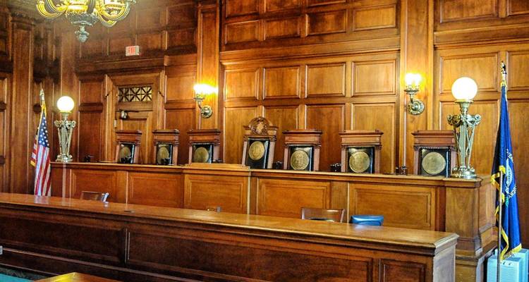 Sala de tribunal con paneles de madera, un estrado elevado para el juez, lámparas de latón y banderas estadounidenses.