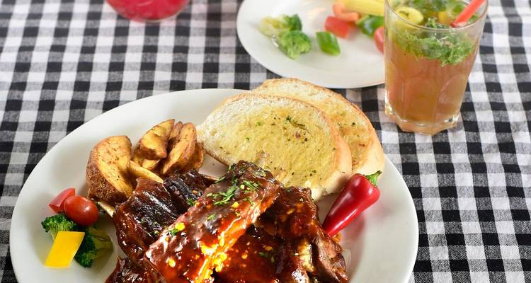 Plato de costillas a la barbecue jugosas con guarniciones y una bebida sobre un mantel a cuadros.
