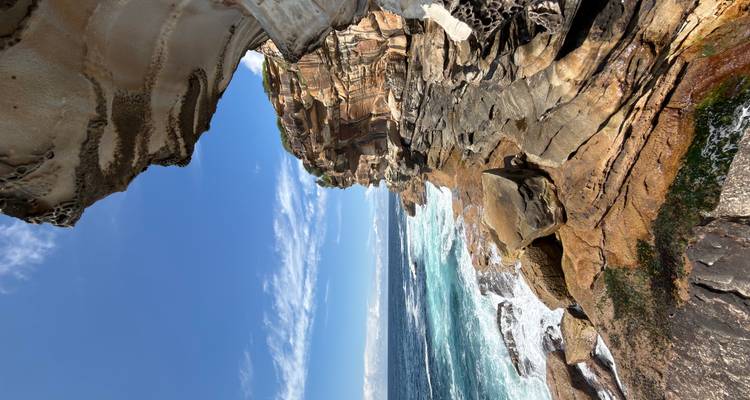 Los acantilados de arenisca texturizada se alzan sobre las olas espumosas a lo largo del camino costero.
