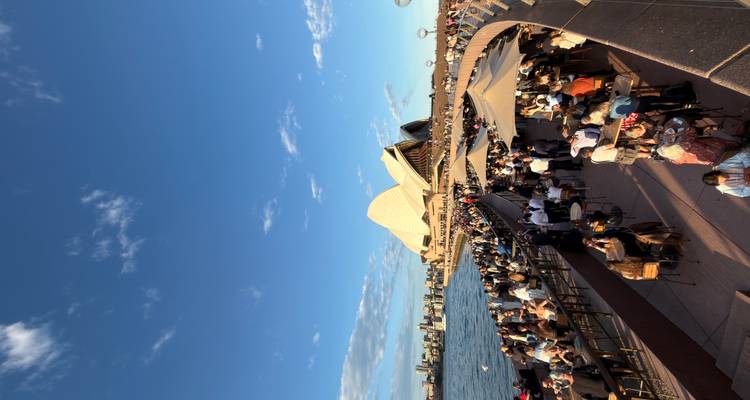Las multitudes disfrutan de bebidas en el Opera Bar con la Ópera de Sídney y el puerto brillante bajo la cálida luz de la tarde.