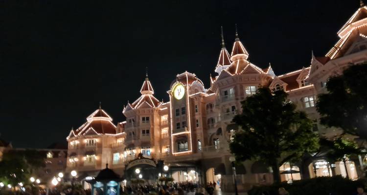 Hôtel Disneyland de style victorien, brillamment illuminé la nuit avec des foules rassemblées devant.