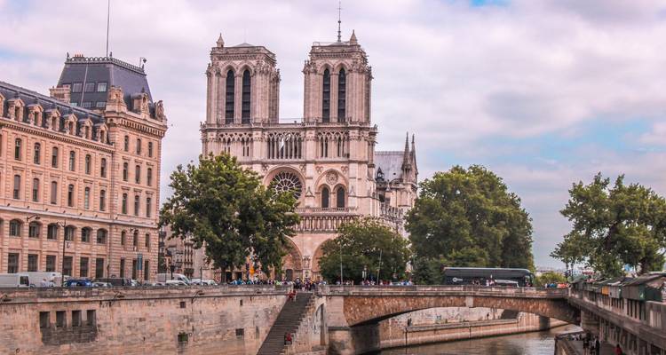 Vue de face de la Cathédrale Notre-Dame avec les quais de la Seine et les piétons traversant un pont.