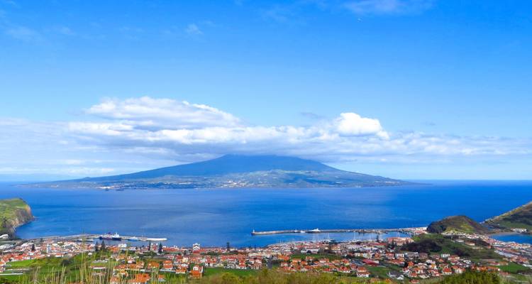 Panoramic view over a seaside town toward Pico Mountain rising above the ocean under blue skies.
