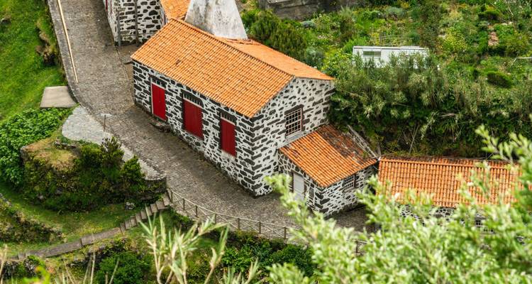 Des maisons en pierre traditionnelles aux toits de tuiles rouges nichées sur un versant vert et escarpé.