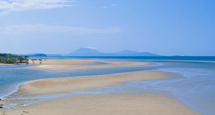 Les vastes bancs de sable et les chenaux de marée peu profonds s'étendent vers des montagnes lointaines et brumeuses sous un ciel bleu.