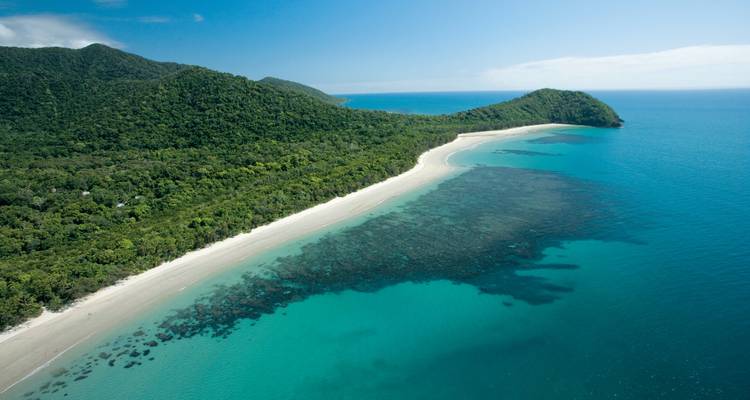 Pristine white-sand beach and coral reef curve around a rainforest-covered headland.