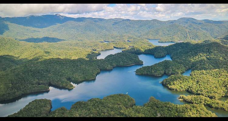 Aerial panorama of winding rainforest lakes set among rolling green mountains.
