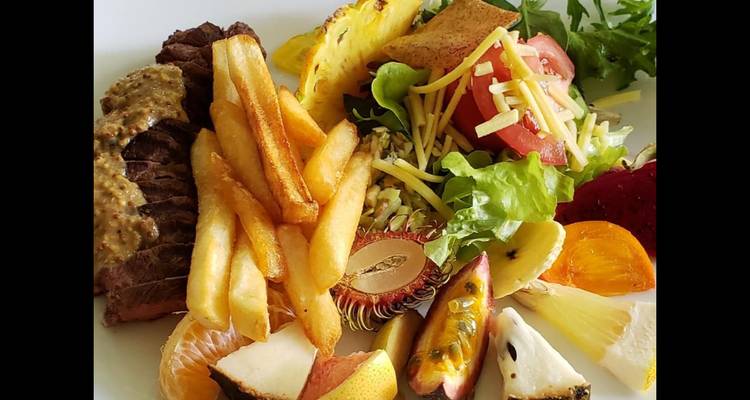 Assiette colorée de steak, frites et fruits tropicaux assortis photographiée sur un fond uni.