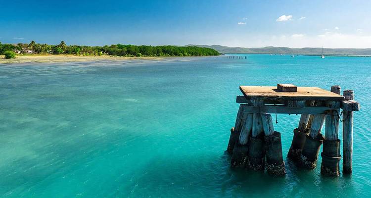 Vestiges d'une vieille jetée en bois s'avançant dans une eau turquoise cristalline près d'un littoral tropical.