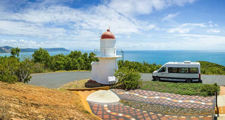 Phare blanc avec un toit rouge à côté d'un camping-car surplombant un vaste panorama océanique bleu.