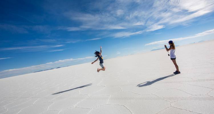 El viajero salta alegremente sobre la corteza blanca y reflectante del Salar de Uyuni mientras su compañero toma fotos.