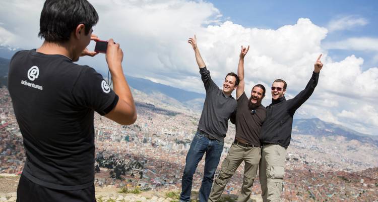 Un viajero fotografía a tres amigos celebrando en la cima de una colina con la ciudad extendida abajo.