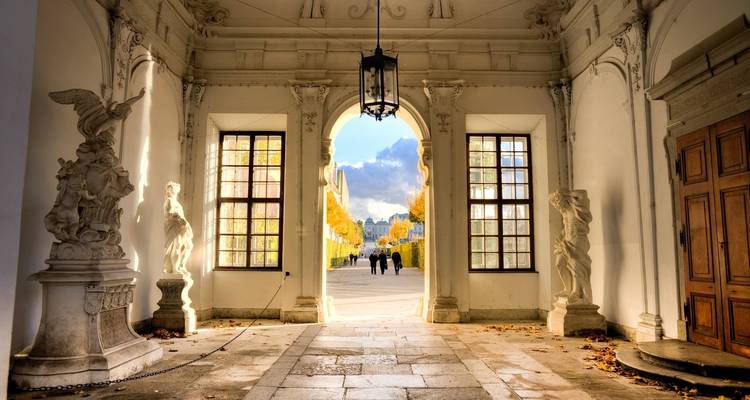 Pasillo elegante en un palacio con estatuas y vista al exterior.