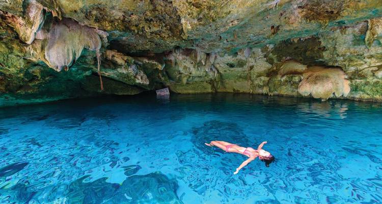 Un nadador flota serenamente en el agua azul cristalina de una cueva cenote de piedra caliza.