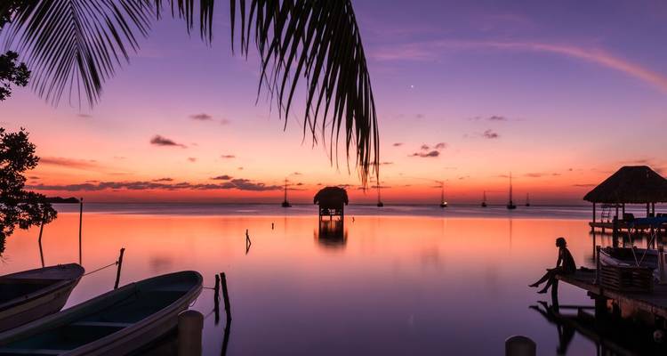 Coucher de soleil serein sur l'eau avec des bateaux en silhouette.