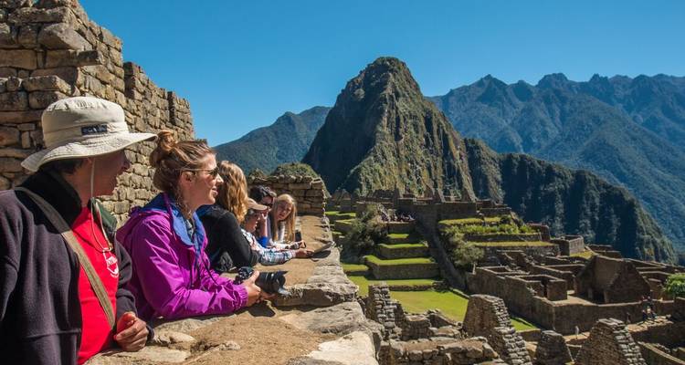 Tourists admire the dramatic ruins of Machu Picchu with jagged Andean peaks behind.