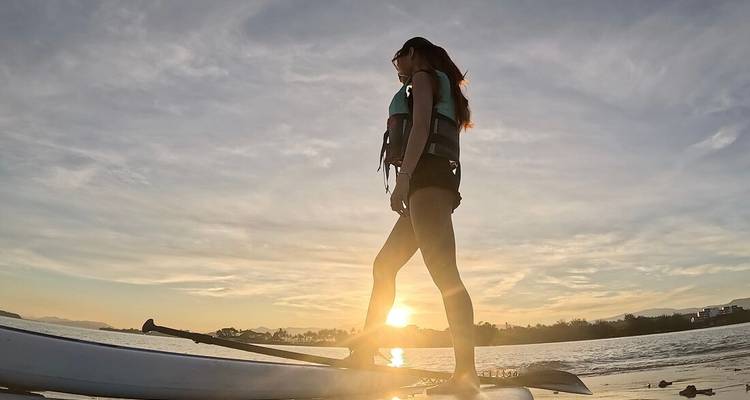 Persona haciendo paddleboard en un mar tranquilo al atardecer.
