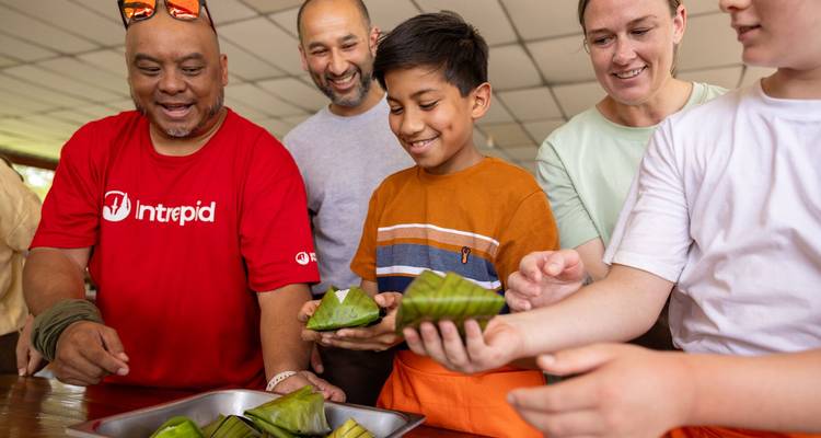 Grupo de viajeros aprendiendo a envolver comida en hojas verdes durante un taller de cocina interactivo.