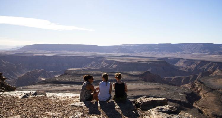 Personas sentadas al borde de un gran cañón con una vista panorámica.