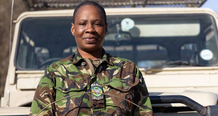Garde forestière souriante en uniforme de camouflage debout devant un véhicule de safari.