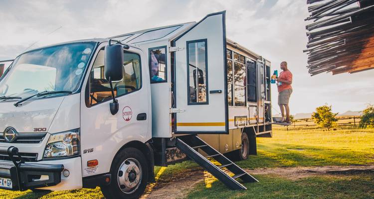 Personas interactuando cerca de un camión de turismo estacionado en un área con césped.