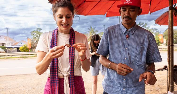 Una mujer y un hombre probando comida local bajo sombrillas rojas.