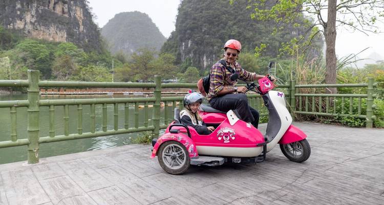 A man and a child on a pink scooter with scenic hills in the background.